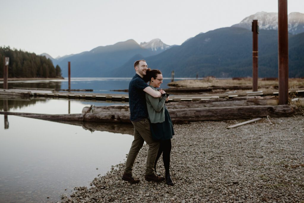 Smiling couple hugging each other at an engagement photo location with mountains in the background at Pitt Lake, Vancouver.