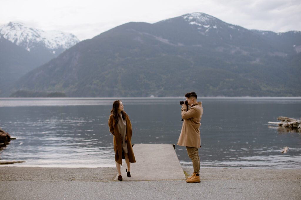 A couple taking each other's photograph at Porteau Cove Provincial Park, a popular engagement photo location in Vancouver.