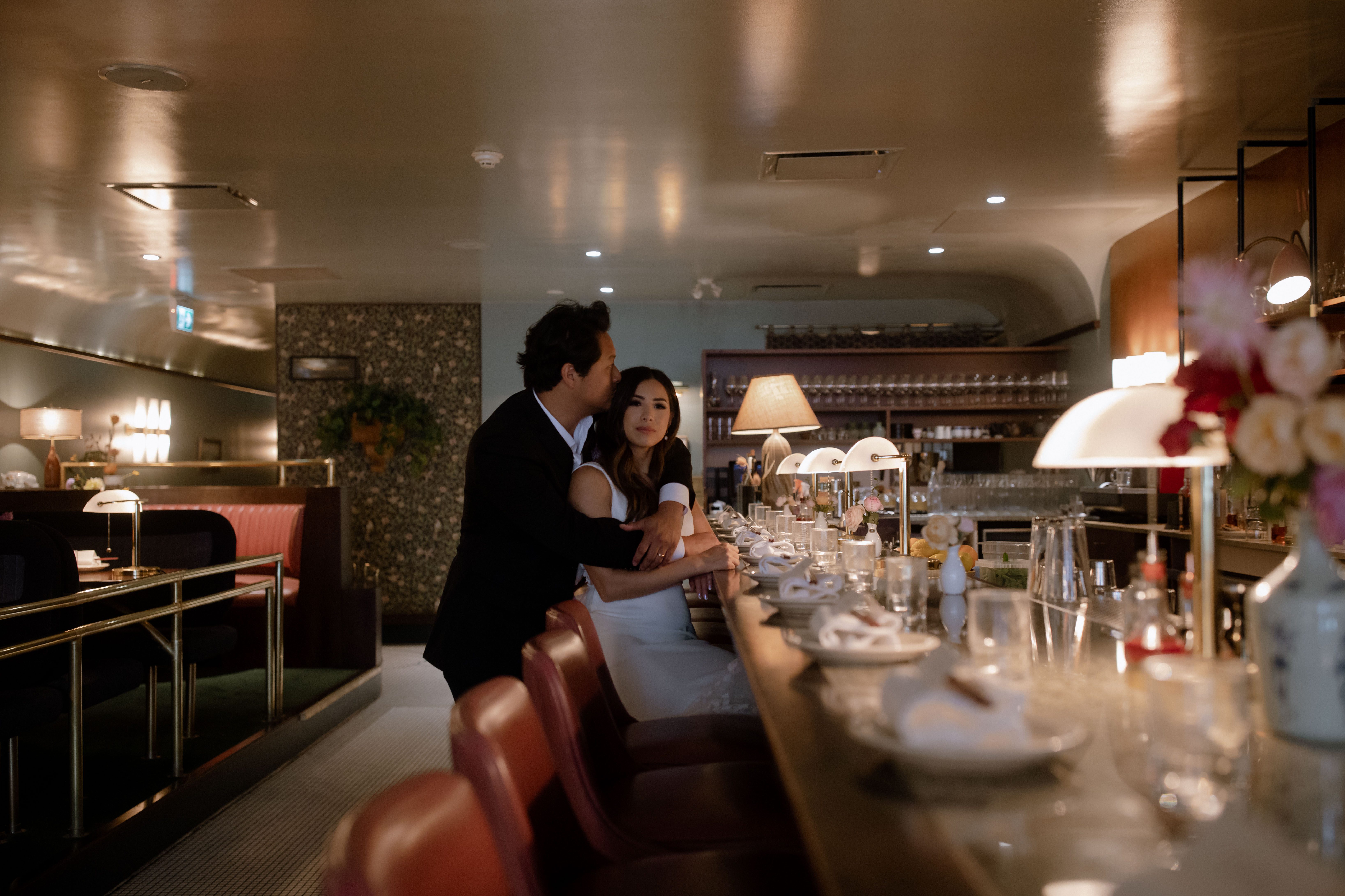 A groom hugging his bride from behind sitting at the bar in Kissa Tanto