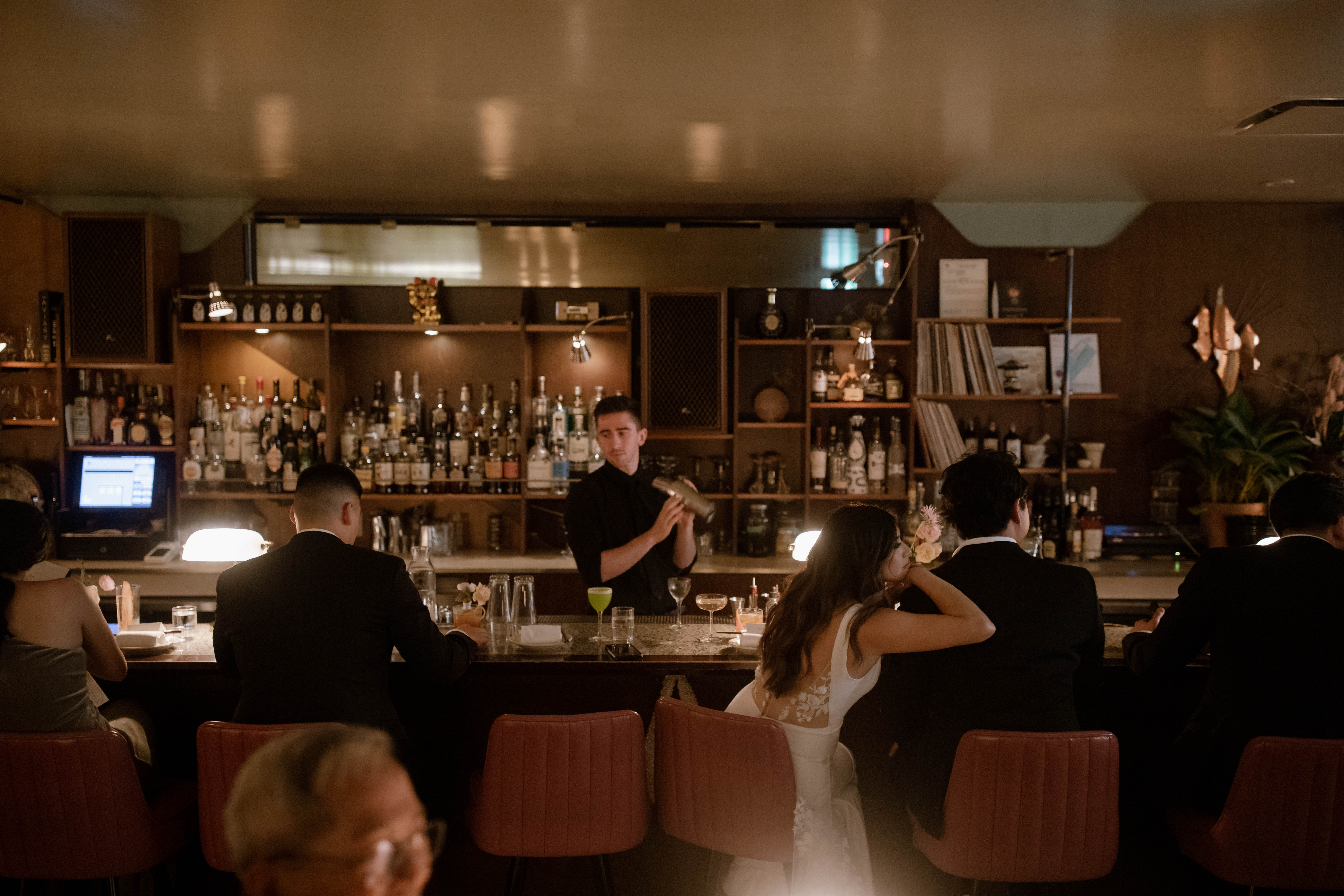 Bride resting her head on groom's shoulder while sitting at the bar in Kissa Tanto