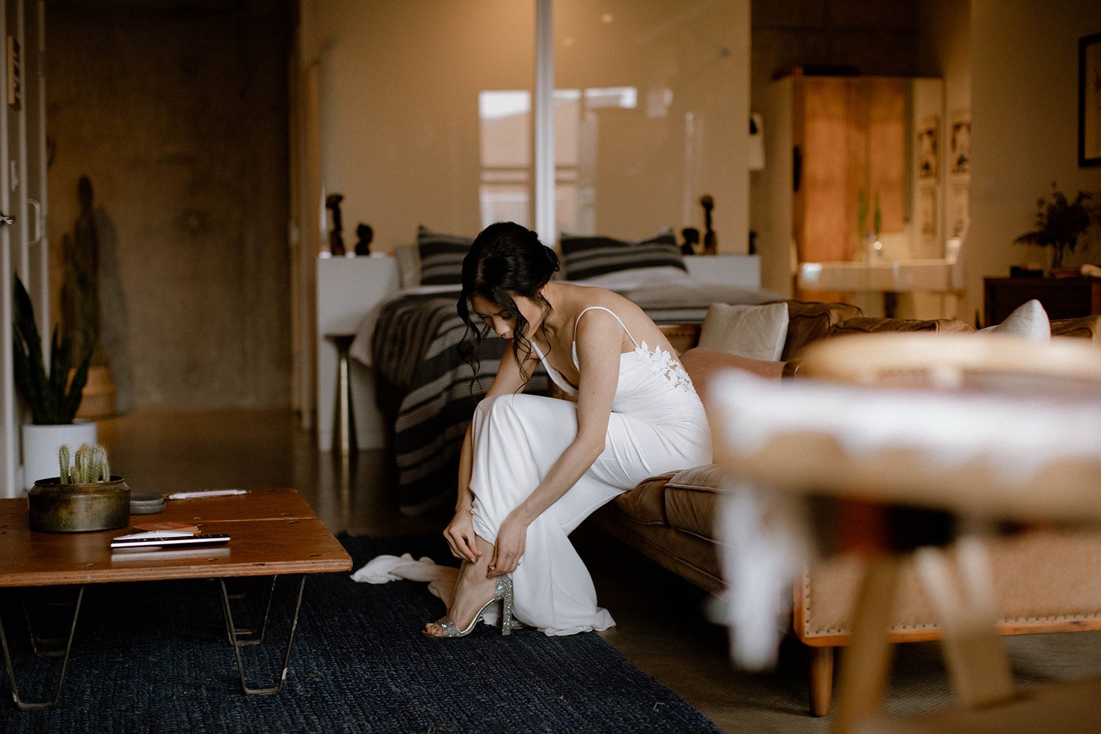 Bride sitting on a couch in a Gastown loft, putting on her sparkly heels.