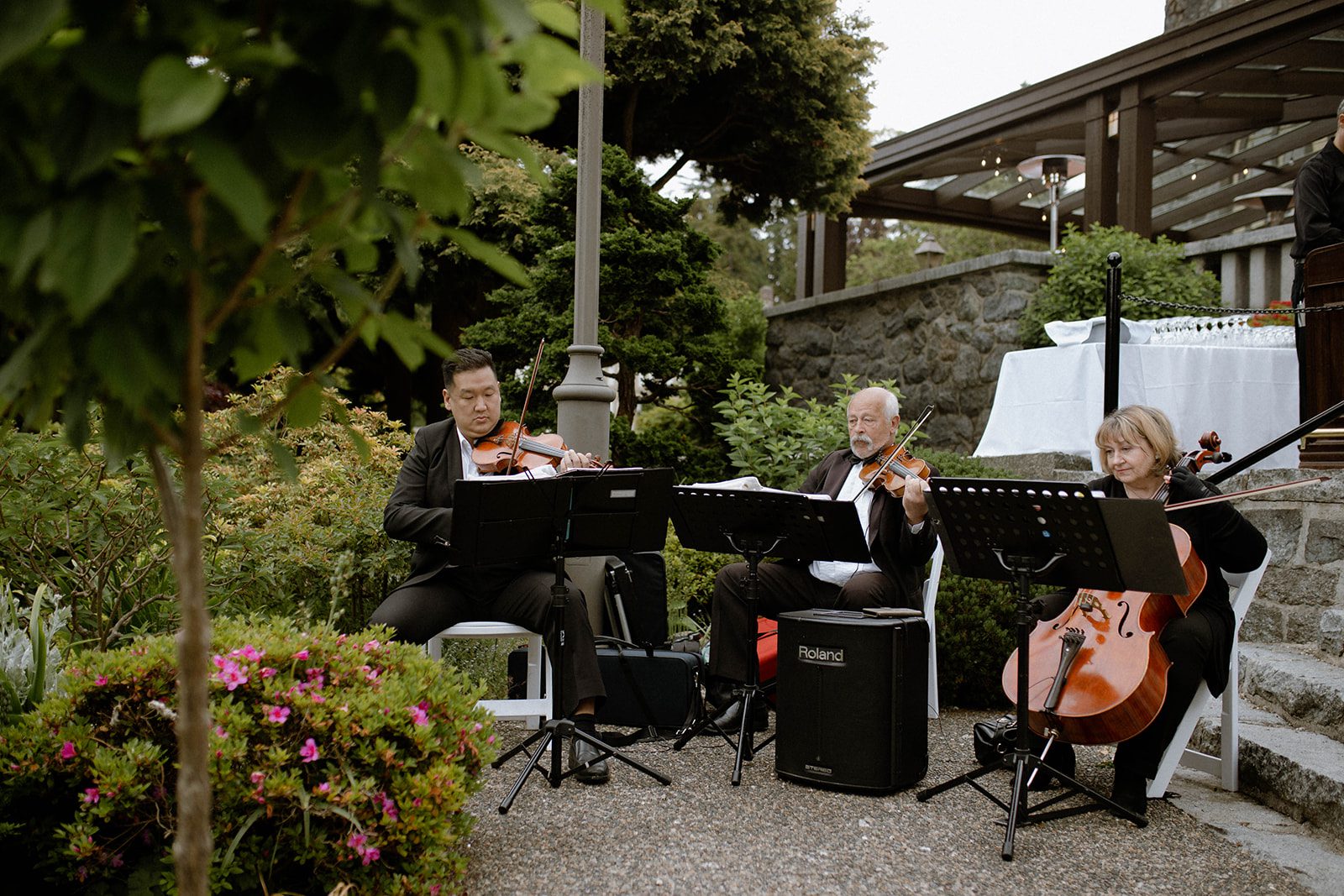 Two violinist and a cellist performing outside of Cecil Green Park House by a flight of stairs.