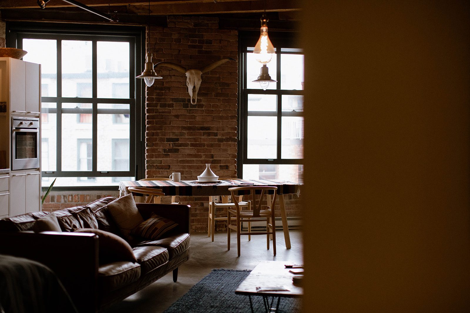 Living room space with leather sofa, dining table, brick walls and large windows.