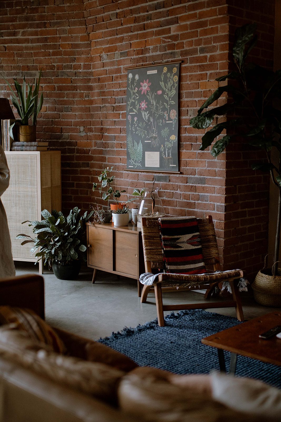 Living Room with brick wall, plants, wooden sideboard, woven chair and a rustic rug in a Gastown Loft.