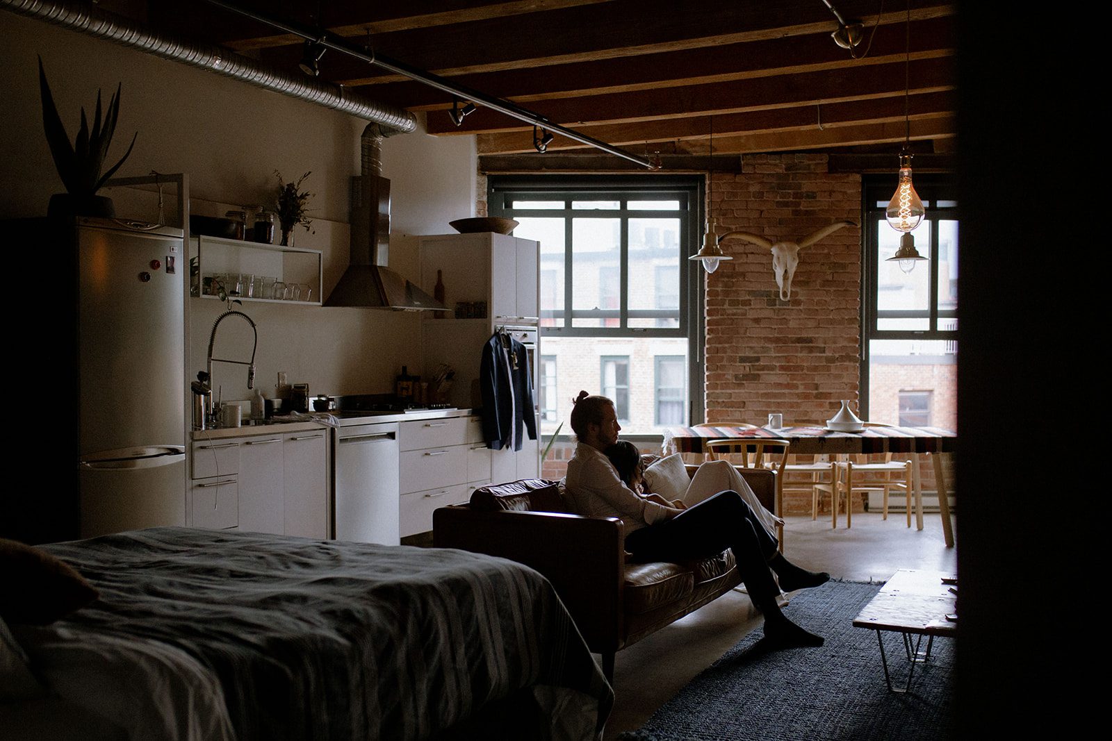 Bride laying on groom sitting on a leather couch in a Gastown loft.