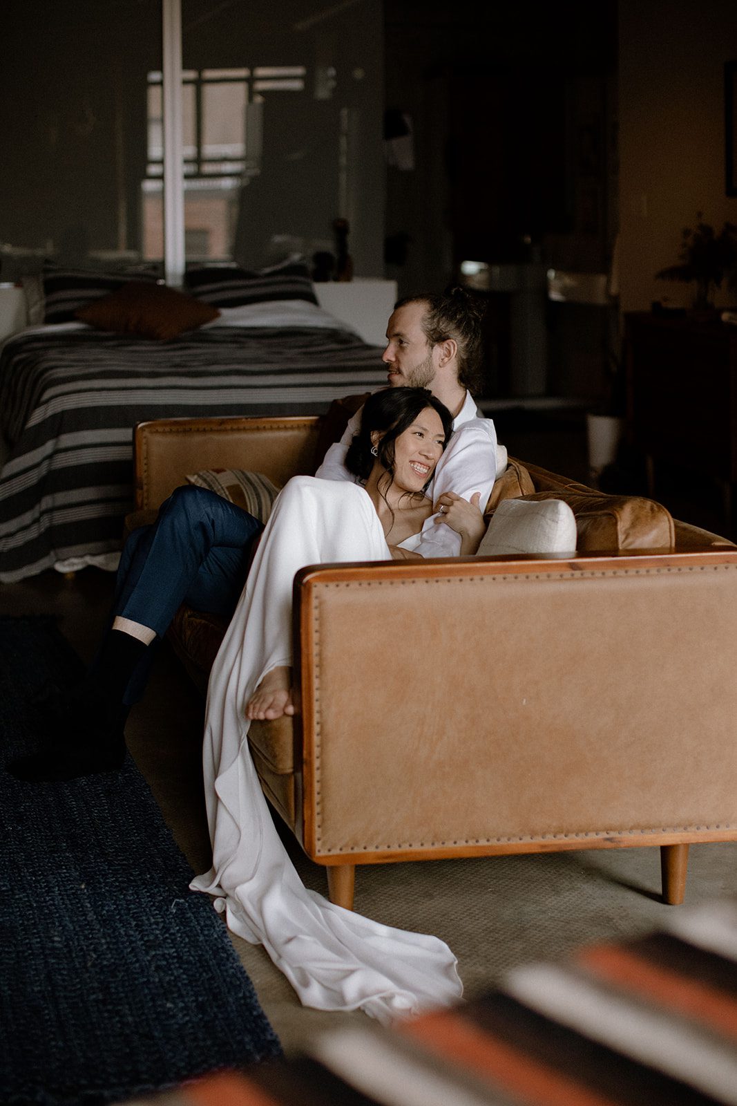 Bride smiling with her feet on the couch while laying on the groom’s shoulder.