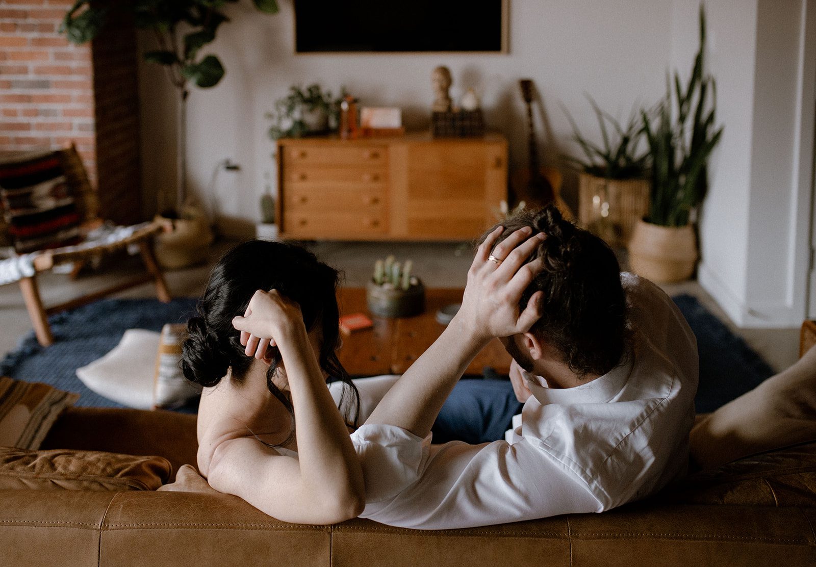 Bride and groom sitting on a couch, facing each other with hands on their heads in a rustic Gastown loft.